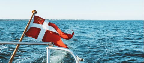 The Danish flag or Dannebrog with a white cross on field of red flies on a boat