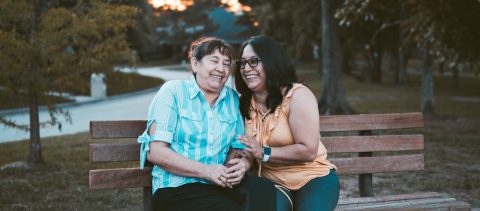 Two women sitting on a park bench laughing