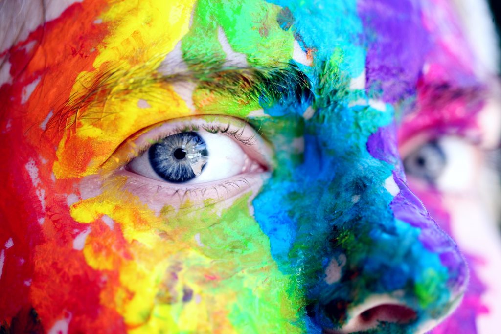 Close up of blue eyes with rainbow paint on face synonymous with LGBTQ movement