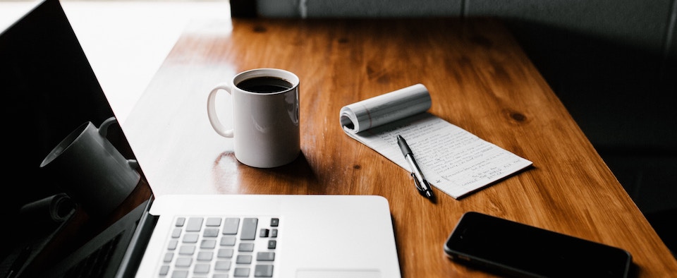 A desk with a notebook computer and coffee to represent working hard on to select the right target accounts