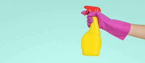 A hand in pink gloves ready to spray some cleaning product